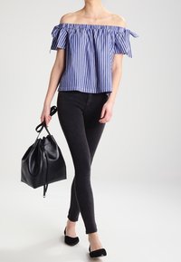 Bluzka w paski bez ramiączek z falbaniastego materiału, w zestawieniu z czarnymi obcisłymi dżinsami, nosząc czarną torebkę w kształcie wiadra i czarne baleriny.