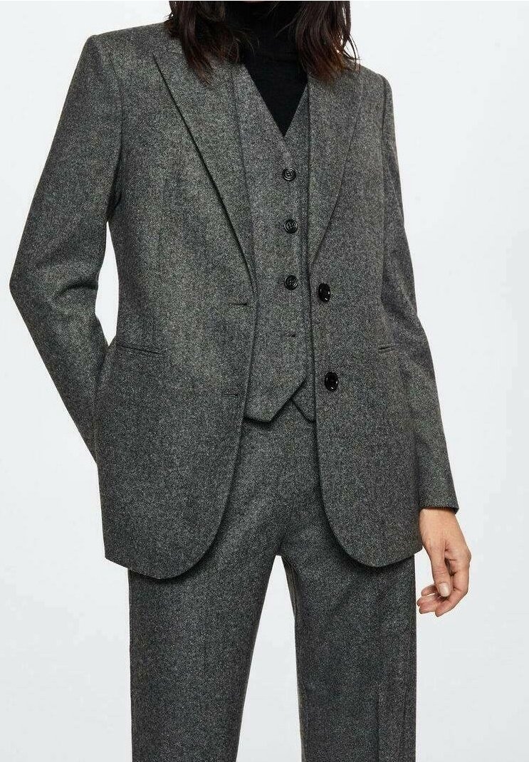 Personne portant un costume trois pièces gris avec blazer, gilet et pantalon, associé à un col roulé noir en dessous.