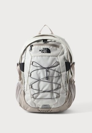 Zaino North Face beige chiaro con tasca frontale con cerniera, cordino elastico bungee, tasche laterali in rete e spallacci imbottiti, vista frontale.