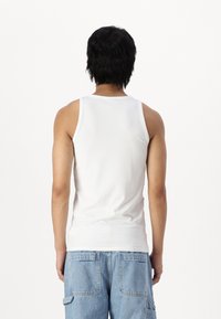 Hvit bomullstank topp med et klassisk design, som har brede skulderstropper og en tettsittende silhuett, kombinert med lyseblå cargo shorts.