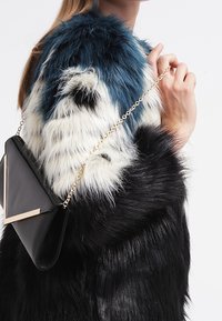 Umělá kožešinová bunda v modré, bílé a černé barvě; hladká textura. Černá kožená kabelka se zlatým řetízkem a ostrými zlatými akcenty.