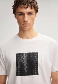 Witte katoenen T-shirt met een zwart rechthoekig grafisch ontwerp met herhaalde tekst "JOOP! JEANS" in verschillende opaciteiten. Klassiek ontwerp met ronde hals.