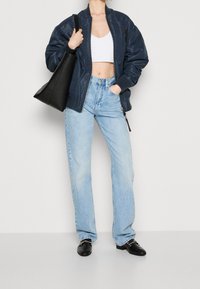 Chaqueta de piloto navy, top corto blanco, jeans rectos azul claro, bolso de cuero negro y zuecos negros con acentos plateados.