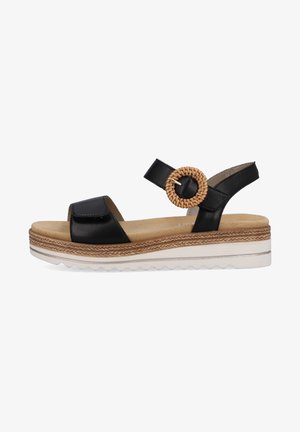 Sandale en cuir noir avec un anneau accent tressé, sangle ajustable, semelle intermédiaire en liège et semelle extérieure en caoutchouc blanc texturé.
