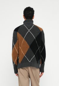 Σκούρο γκρι πουλόβερ με σχέδιο αρπάγκελ, που παρουσιάζει καφέ, μαύρα και λευκά διαμαντένια σχήματα, με ψηλό ριμπ κολάρο και υφή πλέξης.