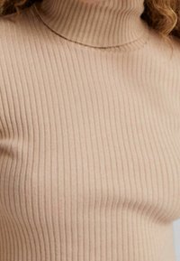 Hladký rolák v světle béžové barvě, vyrobený z měkkého materiálu. Má přiléhavý střih s vertikálními pruhy.