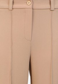Pantalones de tela beige ajustados con una textura suave, cierre de un solo botón y dos bolsillos laterales con detalles de costura.