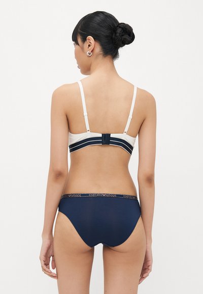White and navy lingerie set, featuring a sleek design. The bra has adjustable straps and a striped band, while the panties showcase an embroidered logo waistband.