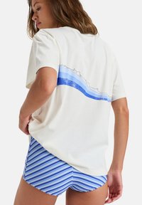 Krämfärgad t-shirt med blå vågmotiv på baksidan, ihopparat med blå och vita randiga shorts. Mjuk bomullsstruktur, avslappnad passform.
