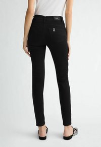 Pantalones vaqueros negros ajustados con una cintura alta, que cuentan con una textura suave, un diseño clásico de cinco bolsillos y una sutil marca en la cinturilla.