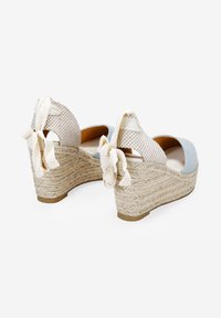 Esparteñas de cuña de tela azul con suelas de yute, que presentan un patrón a cuadros, parte trasera abierta y lazos decorativos beige en el talón.