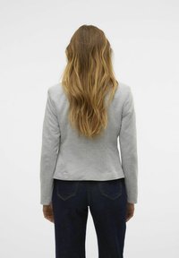 Chaqueta gris ajustada con mangas largas, textura suave y un corte ligeramente cropped, combinada con vaqueros azul oscuro, vista desde la parte trasera.