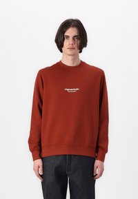 Rustkleurige sweater met een ronde hals, lange mouwen en ribgebreide boorden. Bevat de tekst "Originals Studio" op de borst.