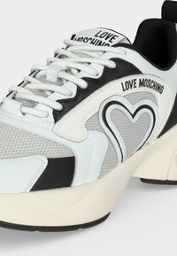 Λευκό και μαύρο sneaker Love Moschino με σχέδιο καρδιάς, δέσιμο μπροστά, πάνελ από δίχτυ και δέρμα και παχιά κρεμώδη σόλα.