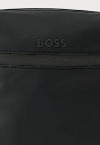 Μαύρη τσάντα από νάιλον με ανάγλυφο λογότυπο "BOSS", λεία υφή, διακριτικές ραφές και κλείσιμο με φερμουάρ. Συμπαγής και πρακτικός σχεδιασμός.
