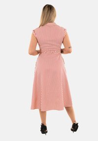 Czerwona i biała w paski sukienka bez rękawów z dopasowanym górą, wiązanym w talii i zwiewnym dołem. Czarne buty na obcasie dopełniają całość.