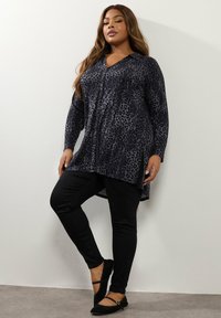 Blusa a maniche lunghe con stampa leopardata scura, scollo a V, dettagli a bottoni e spacchi laterali, abbinata a jeans skinny neri e ballerine nere.