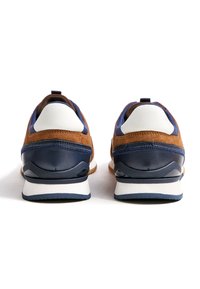 Retro sneakers met bruine suède, marineblauwe leren accenten, witte hielstukjes en een gevoerde zool. Achteraanzicht dat het kleurcontrast benadrukt.