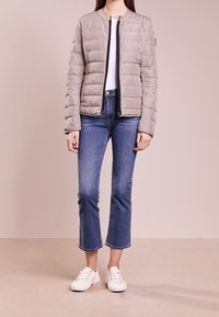 Ljusgrå puffjacka med horisontell sömnad, dragkedja fram och svart trim. Matchad med blå cropped jeans och vita sneakers.