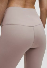 Legginsy wysoko elastyczne w miękkim, stonowanym różu. Gładka tekstura z wzmocnionymi szwami i subtelnym logo z tyłu. Dopasowane w talii i w biodrach.