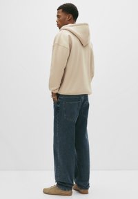 Beige kapucnis pulcsi, laza szabással, sötétkék, bő szárú farmerszoknyával párosítva. Az outfiten finom varrások és oldalsó zsebek találhatók.
