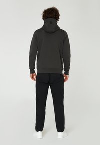 Sudadera gris oscuro con cuello alto y capucha ajustable, combinada con pantalones negros y zapatillas blancas. Textura suave y diseño minimalista.