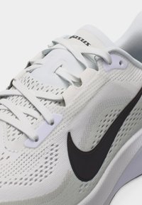 Λευκό παπούτσι τρεξίματος Nike με μαύρο λογότυπο swoosh, επάνω μέρος από δίχτυ για αναπνοή και λευκά κορδόνια δεμένα σε ανοιχτό φόντο.
