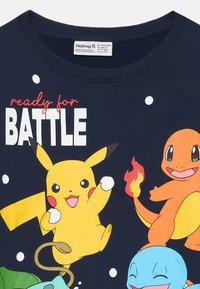 La camiseta azul marino presenta personajes de dibujos animados coloridos: Pikachu, Charmander y Squirtle, con el texto "listo para la BATALLA" y puntos blancos.