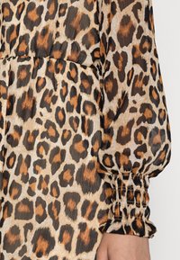Leopardmönstrad blus med jordnära fläckar på en ljusbeige bakgrund, med puffärmar och rynkade manschetter för textur.