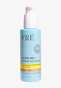 Lichtblauwe fles met een witte pomp; gelabeld "FRÉ GLOW ME + Lichte Getinte Moisturizer," bevat SPF 30, bedoeld voor Medium-Diepe huidtinten.