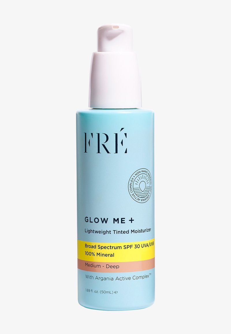 Lichtblauwe fles met een witte pomp; gelabeld "FRÉ GLOW ME + Lichte Getinte Moisturizer," bevat SPF 30, bedoeld voor Medium-Diepe huidtinten.