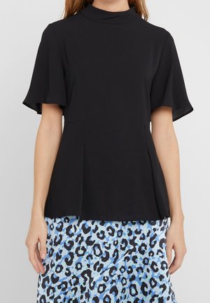 Sort kortærmet bluse med høj hals, der har et flagrende design og sidelommer, parret med en blå leopardmønstret nederdel.