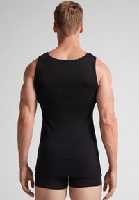 Schwarzes, geripptes Tanktop mit Rundhalsausschnitt, tailliertem Design und breiten Schulterträgern, kombiniert mit schwarzen Shorts; glatte Textur.