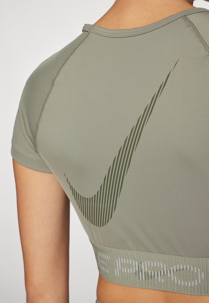 Olivegrünes sportliches Crop-Top mit gerippter Textur, das ein großes, dunkelgrünes Nike-Swoosh-Logo und einen kontrastierenden, strukturierten Saum unten aufweist.