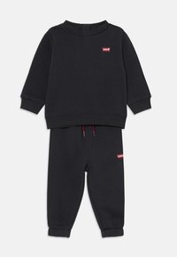 Ensemble en coton comprenant un sweat à capuche noir et un pantalon de jogging assorti, avec des poignets côtelés, un col rond, et un petit logo Levi's rouge sur les deux pièces.