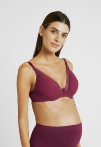 V-shaped burgundy bra made of smooth fabric, featuring lace trim, adjustable straps, and a small decorative center bow.