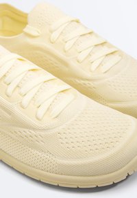 Light yellow knit fabric athletic shoes with matching laces and a perforated breathable design on the upper.