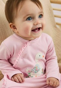 Tutina rosa con pois e bordi arricciati, caratterizzata da un'anatra ricamata con accenti floreali. Tessuto morbido, design casual, maniche lunghe.