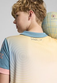 Polo tričko s jemným prechodom farieb, s modrými a ružovými akcentmi. Obsahuje kruhové vzory a ručne písaný text "Definitely City" na chrbte.