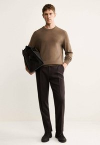 Brauner Strickpullover, dunkle Anzughose, schwarze Tasche mit einem Reißverschlussdetail und schwarze Schuhe. Einfaches Design mit lässiger Passform.