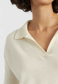 Gestrickter cremefarbener Pullover mit geripptem Kragen und V-Ausschnitt. Weiche Textur mit lockerer Passform, die einen minimalistischen Stil unterstreicht.