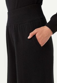 Svarta stickade byxor med bred midja och sidofickor. Tyget verkar mjukt med en slät yta och subtil stretch.