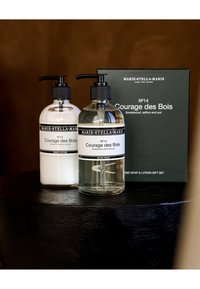 Bouteilles de savon liquide transparent et de lotion blanche avec des distributeurs à pompe noirs, étiquetées "Courage des Bois." Comprend une boîte-cadeau verte foncée.