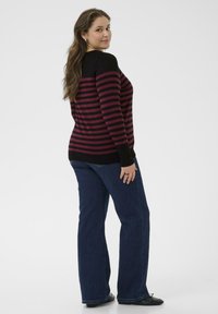 Pull longs en rayures noires et bordeaux avec un corps ajusté et un ourlet évasé, associé à un jean droit en denim bleu et des chaussures noires.