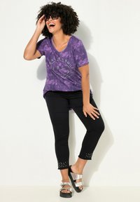 Camiseta de tie-dye púrpura con el texto "Give a Smile" adornado con piedras brillantes, combinada con pantalones negros con dobladillo studded y sandalias plateadas.