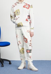 Sudadera y pantalones blancos con gráficos coloridos, incluyendo "23", cinturones dorados y acentos rojos. Usados con zapatillas blancas.