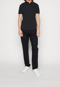 Černé polo tričko s fialovými akcenty na límci, kombinované s černými kalhotami a bílými teniskami. Fit je neformální a elegantní.