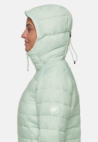 Lichtgroene pufferjas met een capuchon, met een gequilt ontwerp en een ritsluiting. Logo op de mouw, verstelbaar trekkoord bij de capuchon.