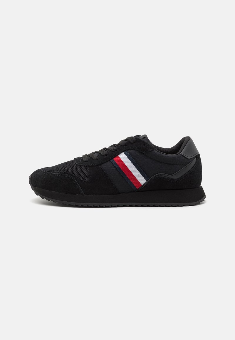 Baskets basses noires avec semelle et lacets noirs, avec un détail en tissu rayé rouge, blanc et bleu sur le côté.