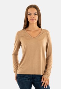 Lange mouw, V-hals top in lichtbruine stof, met vier knoopaccenten op de borst. Gecombineerd met donkerblauwe jeans, met een gladde textuur en een relaxte pasvorm.